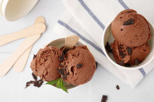 Paper cups with tasty chocolate ice cream on white tiled table, flat lay