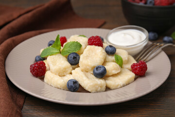 Plate of tasty lazy dumplings with berries, sour cream and mint leaves on wooden table