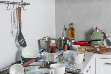 Many dirty utensils, cookware and dishware on countertop in messy kitchen