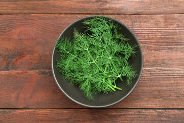 Bowl of fresh green dill on wooden table, top view