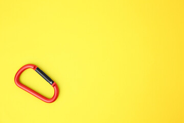 One red carabiner on yellow background, top view. Space for text