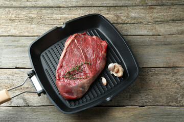 Grill pan with piece of raw beef meat, garlic and thyme on wooden table