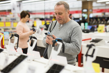 Attentive European man chooses a mobile phone in an electronics store to buy it