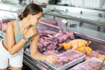 Female customer attentively examines various meat cuts, evaluating their quality and freshness.