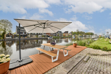 an outdoor area with tables and umbrellas on the side of the water in front of a row of houses