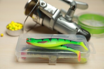 Different fishing baits and reel with line on light wooden table, closeup