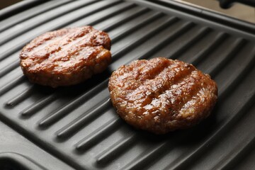 Delicious hamburger patties on electric grill, closeup