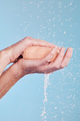 Fototapeta premium Water, soap and a person washing hands in studio on a blue background for hygiene or hydration. Cleaning, wellness and skincare with an adult in the bathroom to remove bacteria or germs for health
