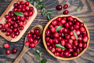 Fresh cranberries in a wooden bowl with spoon on dark wooden table. View from above.