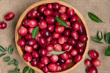 Cranberries in a wooden bowl on a burlap background. View from above. Close-up.