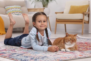 Smiling little girl and cute ginger cat on carpet at home