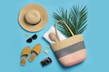 Wicker bag, camera, palm leaves and beach accessories on light blue background, flat lay