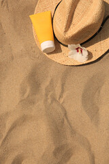 Fototapeta na wymiar Sunscreen, straw hat and flower on sandy beach, top view and space for text. Sun protection