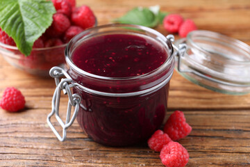 Jar of delicious raspberry jam and fresh berries on wooden table, closeup