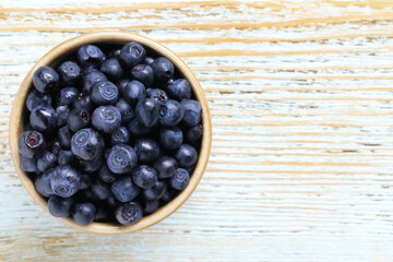 Tasty fresh bilberries in bowl on old light blue wooden table, top view. Space for text