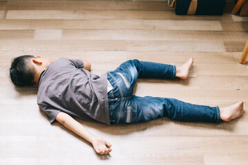 Little boy in casual jeans and t shirt sleeping on wooden floor. Fainted boy - obrazy, fototapety, plakaty