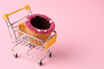 Delicious edible biscuit coffee cup decorated with sprinkles in shopping cart on pink background,...