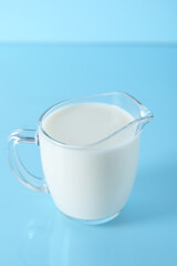 Jug of fresh milk on light blue background