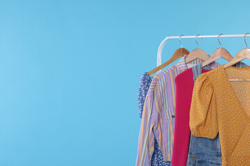 Rack with stylish women`s clothes on wooden hangers against light blue background, space for text