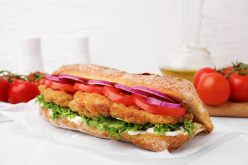 Delicious sandwich with schnitzel on white tiled table