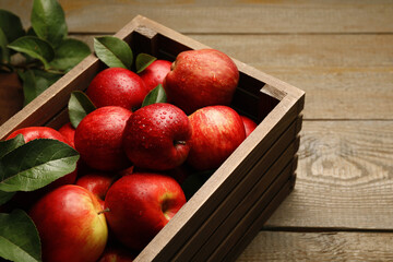 Ripe red apples with water drops in crate and green leaves on wooden table