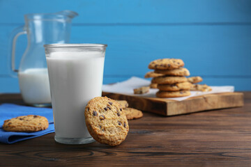 Delicious chocolate chip cookies and glass of milk on wooden table, space for text