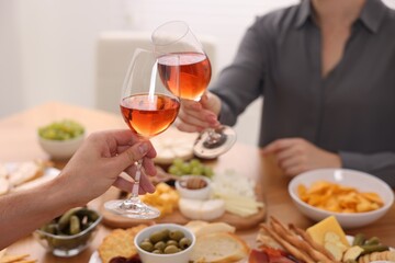 People clinking glasses with rose wine above table indoors, closeup