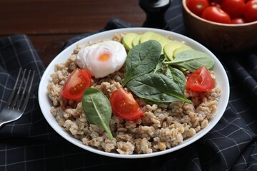 Delicious boiled oatmeal with poached egg, tomato, avocado and fork on table, closeup