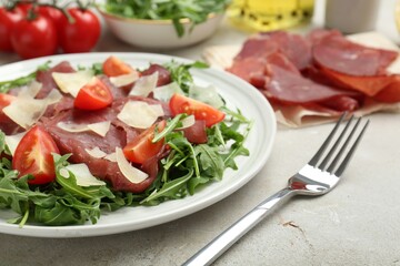 Delicious bresaola salad with parmesan cheese served on light grey textured table, closeup