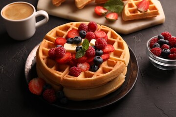 Tasty Belgian waffles with fresh berries, cheese and cup of coffee on black table, closeup