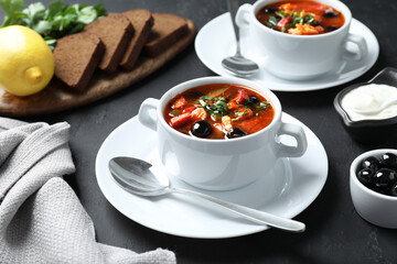 Meat solyanka soup with sausages and olives served on dark grey textured table