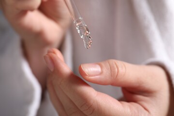 Woman applying cosmetic serum onto finger, closeup view