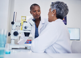 Women, science and discussion of team at microscope for research, medical analysis and biotechnology in laboratory. Black woman listening to scientist for microbiology investigation, dna test or plan