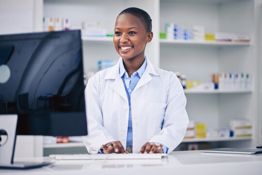 Pharmacist, Typing And Happy Black Woman On Computer In Pharmacy, Drugstore Or Shop. Smile, Medical Professional And African Doctor On Internet For Telehealth, Healthcare And Research For Medicine.