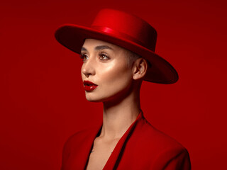 Vision, fashion and a model woman on a red studio background for elegant or trendy style. Aesthetic, art and hat with a young female person looking edgy or classy in a suit or unique clothes