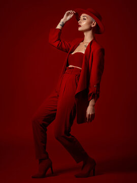 Art, fashion and a model woman on a red studio background for elegant or trendy style. Aesthetic, beauty and bold with a young female person looking edgy or classy in a suit walking on the runway