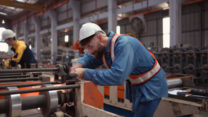 A team of factory technician use a wrench to inspect the conveyor belt of the metal sheet production machine.