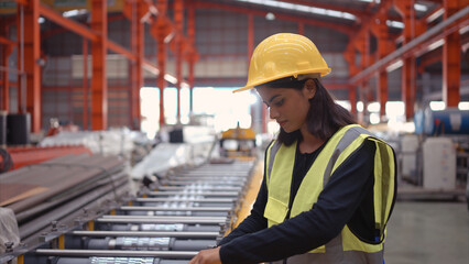 A female factory technician use a wrench to inspect the conveyor belt of the metal sheet production machine. - obrazy, fototapety, plakaty