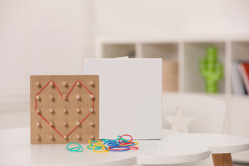 Wooden geoboard with rubber bands on white table indoors. Educational toy for motor skills development