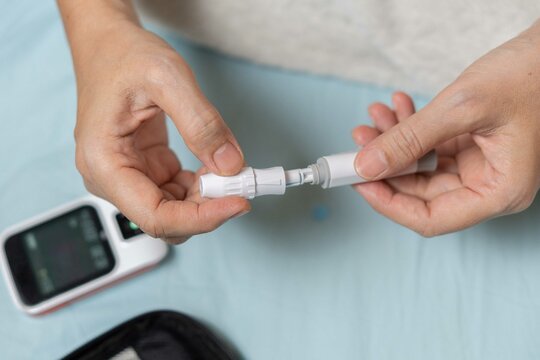 A woman's hand checking her blood sugar level with a glucometer by herself at her home. SHOTLISThealth - Powered by Adobe