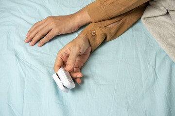 Female's hands with a pulse oximeter at the index finger. Woman lying at the bed. Gadgets for...