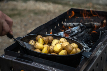 Cooking on a grill, in cast iron cookware, outdoors. Rural food, potatoes with lard.