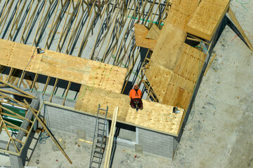 Aerial view of builders working on unfinished residential house with wooden roof frame structure under construction in Florida suburban area