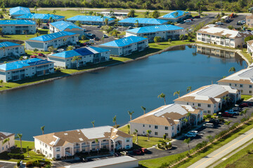 Aerial view of damaged in hurricane apartment building roofs covered with blue protective tarp...