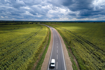 Fototapeta na wymiar Aerial view of intercity road between green agricultural fields with fast driving car. Top view from drone of highway traffic