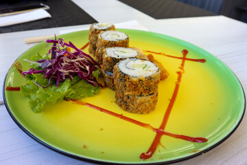 Fried sushi roll served in a serving plate with vegetables. Closed up view of Japanese food