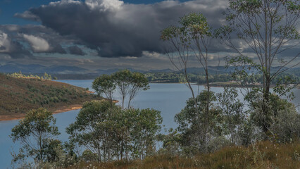 The island is visible in a beautiful blue lake. Green vegetation on the banks - grass, bushes, trees. Picturesque clouds in the sky. Mountains in the distance. Madagascar. Mantasoa Lake
