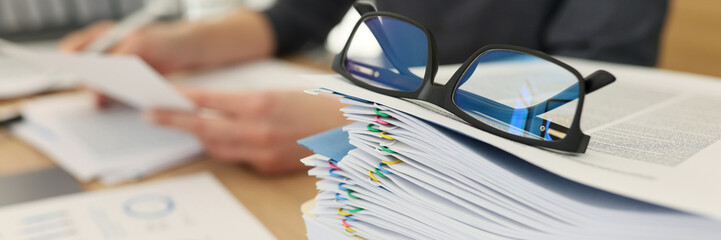 Glasses for eyesight lie on stack of documents at workplace