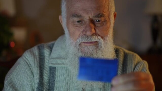 An elderly bearded man with a blue card in his hand carefully checks and enters the data from it