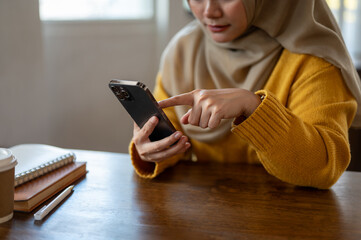 Close-up image of an Asian-muslim woman is using her smartphone while sitting in a coffee shop.